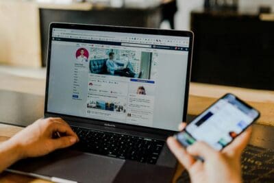 Person using laptop and smartphone to manage social media marketing campaigns.