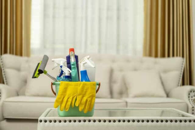 Cleaning supplies and tools in a bucket on a coffee table in a living room.