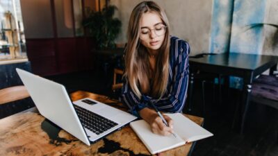 Young woman working on a laptop and notebook, focusing on web design and digital growth strategies.